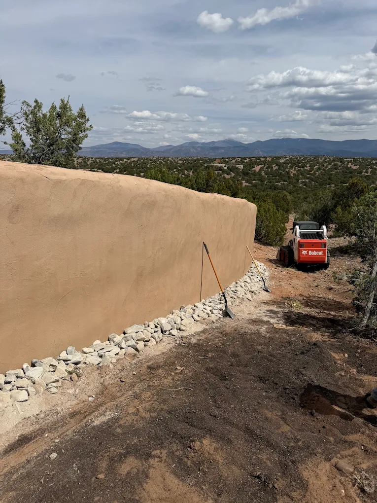 Skid steer beside a stucco wall and freshly graded soil